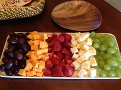 grapes, strawberries, and cheese are arranged in a tray on a wooden table