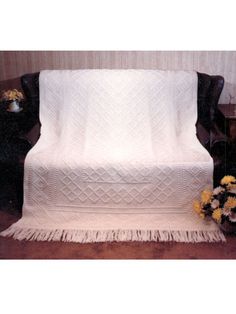 a white blanket sitting on top of a wooden table next to a vase with flowers