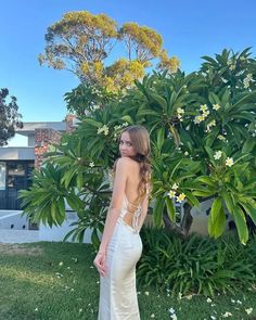 a woman standing in front of a bush wearing a white dress with open back and straps