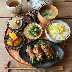 an assortment of food on a plate with chopsticks and tea cups next to it