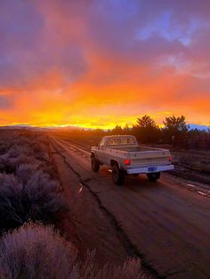 a white truck driving down a dirt road at sunset in the middle of an open field