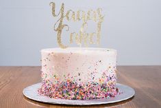 a white cake with sprinkles and a gold happy god topper