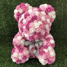 a teddy bear made out of pink and white roses sitting on the ground with grass in the background