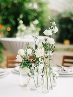 three vases filled with white flowers sitting on top of a dining room table in front of an outdoor setting