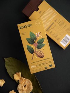 a box of kuyay chocolate next to some leaves and flowers on a table