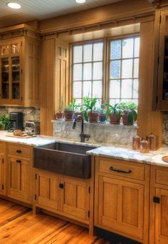 a large kitchen with wooden cabinets and marble counter tops is pictured in this image, there are potted plants on the window sill above the sink