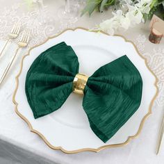 a white plate topped with a green bow tie on top of a table next to silverware