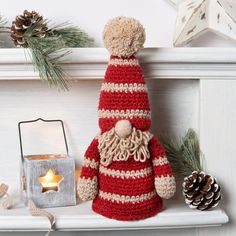 a crocheted santa clause sitting on top of a mantle next to a lit candle