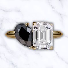 an emerald and black diamond ring on a white marble surface with gold trimmings