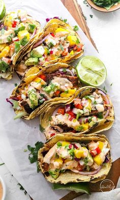 fish tacos with avocado, salsa and limes on a cutting board