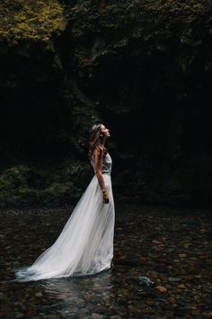 a woman standing in the water wearing a wedding dress