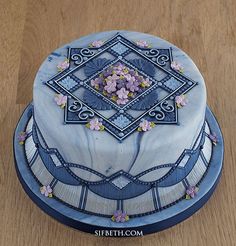 a blue cake with flowers on it sitting on top of a wooden table next to a knife