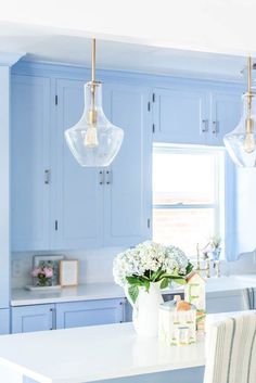 a kitchen with light blue cabinets and white counter tops, two pendant lights over the island