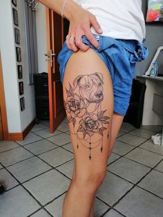 a woman's thigh with a dog and roses tattoo on her leg, next to a tiled floor