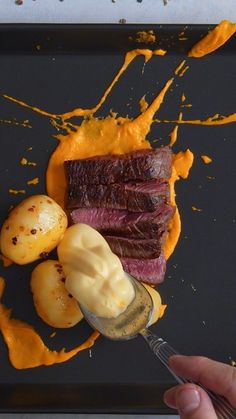 a person is holding a spoon over some food on a black tray with orange sauce