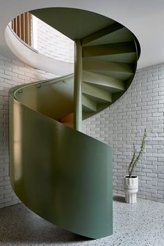 a green spiral staircase next to a potted plant in a white brick wall room