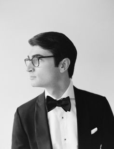 a man in a tuxedo and bow tie looks off to the side while wearing glasses