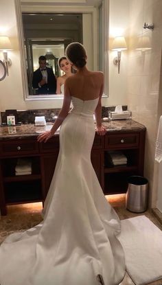 a woman standing in front of a bathroom mirror wearing a wedding dress and looking at herself in the mirror