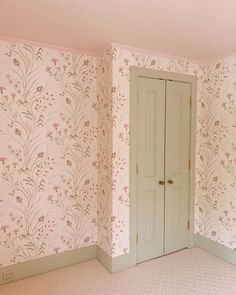 an empty room with floral wallpaper and two doors in the corner that lead into another room