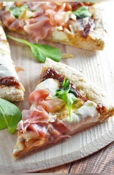 two slices of pizza sitting on top of a wooden cutting board next to green leaves