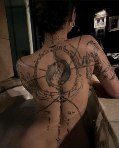 a woman sitting in a bathtub with tattoos on her back