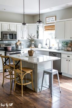 a kitchen with white cabinets and wooden flooring is pictured in this image, there are two stools at the center of the island