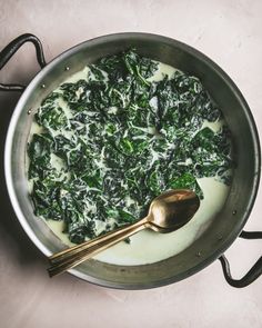 a pot filled with spinach and cheese on top of a counter next to a spoon