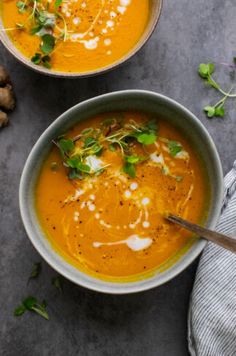 two bowls filled with carrot soup and garnished with fresh herbs on the side