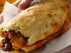 a close up of a person holding a burrito in their hand with cheese and meat on it