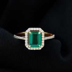 an emerald and diamond ring sitting on top of a black cloth with diamonds around it