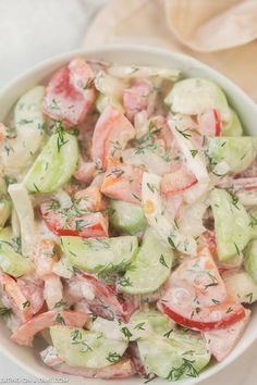 a white bowl filled with cucumber and tomato salad on top of a table