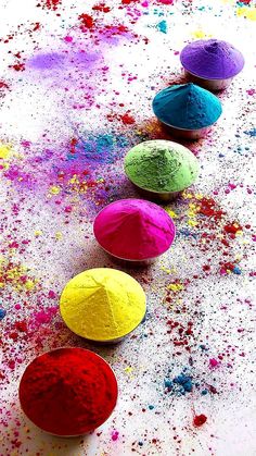 four bowls filled with different colored powders on top of a white floor covered in multicolored paint