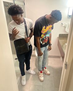 two young men standing in a bathroom looking at their cell phones