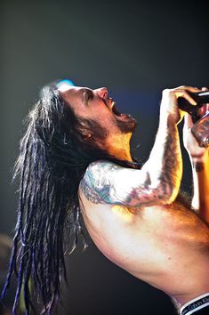 a man with long hair and tattoos on his chest holding a microphone in his hand