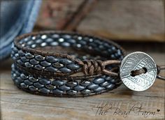 two leather bracelets with silver beads and a coin sitting on top of each other