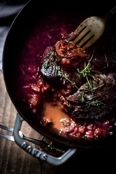 a pan filled with meat and sauce on top of a wooden table next to a fork