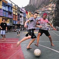 two young men are playing soccer on an outdoor court with mountains in the back ground