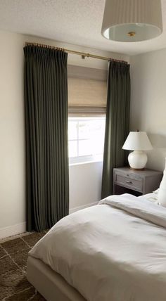 a white bed sitting next to a window in a room with green curtains on the windowsill