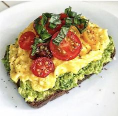 an omelet topped with tomatoes, avocado and spinach on a white plate