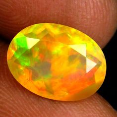 a person holding an orange and yellow opal in their left hand, with the top half