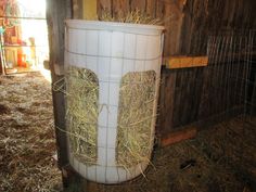 a large white barrel filled with hay next to a wooden fence in a barn area