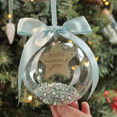 a person holding up a glass ornament with a star on it and a blue ribbon