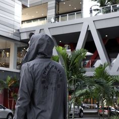 a man walking down the street in front of a building wearing a hoodie and carrying a skateboard