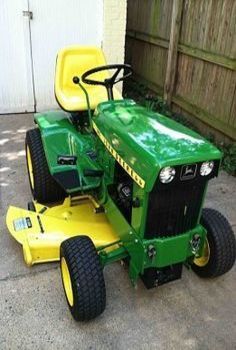 a green and yellow tractor parked in front of a building with a wooden fence behind it