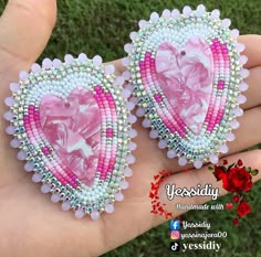 two heart shaped brooches with pink and white beads are held in someone's hand