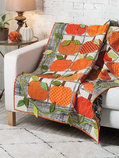 an orange quilt on a white couch next to a table with a lamp and potted plant