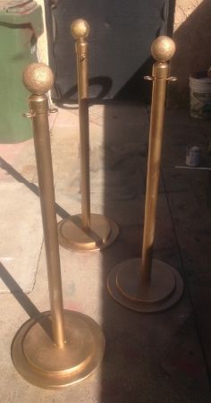 two gold colored candlesticks are standing next to each other on the sidewalk in front of a trash can