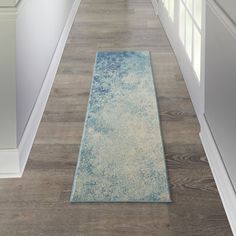 a long hallway with white walls and wooden floors, along with a blue rug on the floor