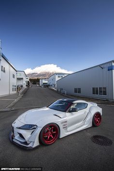 a white sports car parked in front of a building with red rims on it