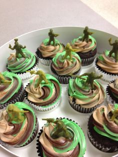 cupcakes decorated with green and brown frosting on a white platter topped with toy figurines